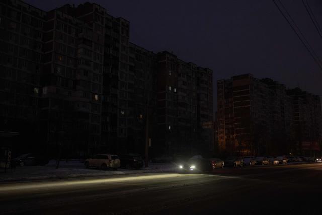 A car drives past darkened apartment buildings on a freezing day during a power outage in a residential neighborhood of Kyiv on January 23, 2026, following Russian missile and drone attacks on Ukrainian energy infrastructure amid the Russian invasion in Ukraine. (Photo by Roman PILIPEY / AFP)