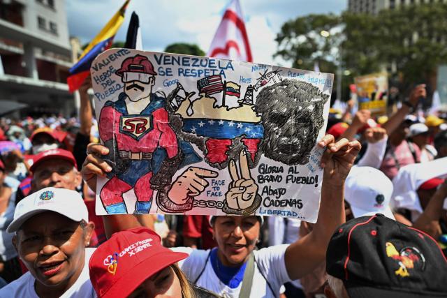 A supporter of ousted Venezuelan President Nicolas Maduro shows a sign depicting him as the character named "Super-Bigote" ("Super-Mustache") during a demonstration calling for the release of him and his wife from a US prison in Caracas on January 23, 2026. Thousands of Nicolas Maduro's supporters marched in Caracas on January 23, calling for the release of the ousted president, as Venezuela marked the 68th anniversary of the fall of military dictatorship. (Photo by Juan BARRETO / AFP)