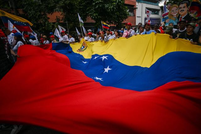 Supporters of ousted Venezuelan President Nicolas Maduro hold a giant national flag during a demonstration calling for the release of him and his wife from a US prison in Caracas on January 23, 2026. Thousands of Nicolas Maduro's supporters marched in Caracas on January 23, calling for the release of the ousted president, as Venezuela marked the 68th anniversary of the fall of military dictatorship. (Photo by Juan BARRETO / AFP)
