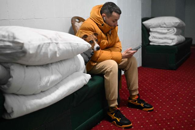 A man with his dog sits on the sofa in the hotel's underground shelter during an air attack in Kyiv early on January 24, 2026, amid the Russian invasion of Ukraine. (Photo by Sergei GAPON / AFP)