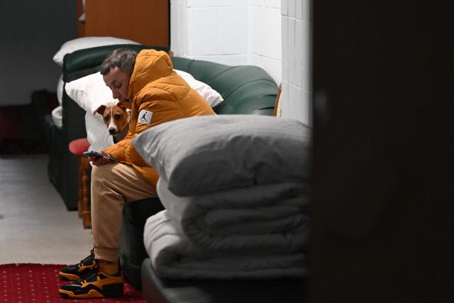 A man with his dog sits on the sofa in the hotel's underground shelter during an air attack in Kyiv early on January 24, 2026, amid the Russian invasion of Ukraine. (Photo by Sergei GAPON / AFP)