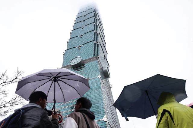 People hold umbrellas under the landmark Taipei 101 building, which US climber Alex Honnold was scheduled to scale but postponed due to bad weather, in Taipei on January 24, 2026. (Photo by I-Hwa Cheng / AFP)