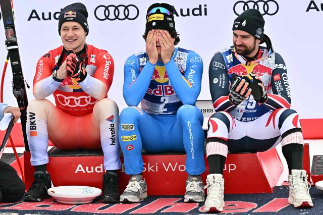 (L-R) Second placed Switzerland's Marco Odermatt, winner Italy's Giovanni Franzoni and third placed France's Maxence Muzaton react on the podium after the Men's Downhill event of the FIS Alpine Skiing World Cup in Kitzbuhel, Austria, on January 24, 2026. (Photo by Joe Klamar / AFP)