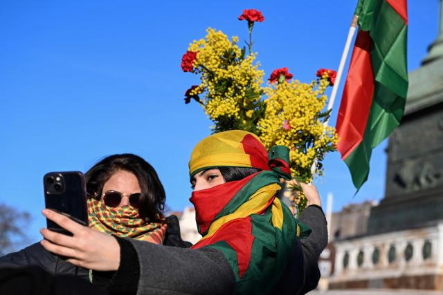 Protesters pose for a selfie pictures with a mimosa bouquet and a pro-Kurdish flag during a demonstration in solidarity with Kurds in northern Syria, in central Paris, on January 24, 2026. More than 134,000 people have been displaced in northeast Syria, according to the United Nations said on January 22, after clashes and a fragile ceasefire deal between government troops and the Kurdish-led Syrian Democratic Forces (SDF). (Photo by Blanca CRUZ / AFP)
