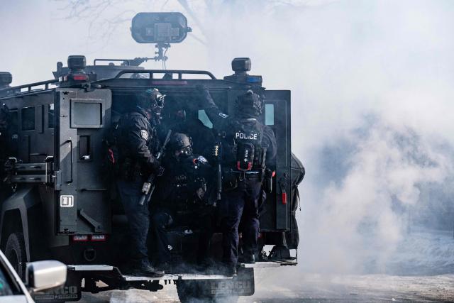 Minneapolis police officers ride an armored vehicle after releasing gas canisters at protesters near where a man was shot dead by federal immigration agents in Minneapolis, Minnesota, on January 24, 2026. Federal immigration agents shot dead a man in Minneapolis on Saturday, officials said -- the second fatal shooting of a civilian in the city, sparking fresh protests and outrage from state officials. The death came less than three weeks after US citizen Renee Good was shot and killed by an Immigration and Customs Enforcement officer involved in sweeps to round up undocumented migrants. (Photo by ROBERTO SCHMIDT / AFP)