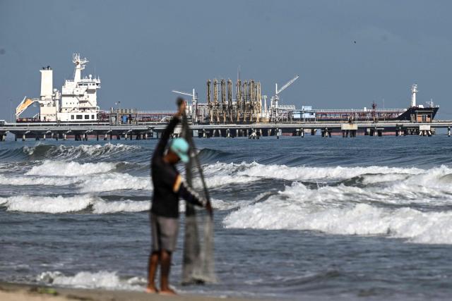 (FILES) A fisherman stands by the sea as a tanker is docked at the El Palito refinery pier, in Puerto Cabello, Carabobo state, Venezuela on January 22, 2026. Venezuela wants to boost its oil production by 18 percent this year through planned reforms that will fully open the sector to private investors, the head of the state oil giant PDVSA said on January 24, 2026. (Photo by Ronaldo SCHEMIDT / AFP)
