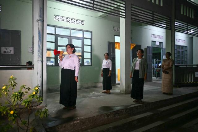 A volunteer (L) from the Union Election Commission (UEC) uses a loudhailer to announce the opening of polls on the third and final phase of Myanmar's general election, at a polling station in Yangon on January 25, 2026. Myanmar opened the final round of its month-long election on January 25, with the dominant pro-military party on course for a landslide in a junta-run vote critics say will prolong the army's grip on power. (Photo by Sai Aung MAIN / AFP)