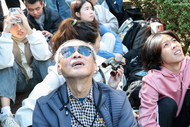 A reflection of the Taipei 101 building is seen in an onlooker's sunglasses as people watch US rock climber Alex Honnold scale the landmark skyscraper without ropes or safety gear in Taipei on January 25, 2026. (Photo by I-Hwa Cheng / AFP)