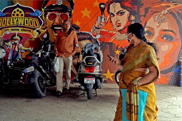 (FILES) This photograph taken on July 21, 2020 shows people walking past a wall mural with images of Bollywood actors, under a road bridge in Mumbai. India's Bollywood is moving decisively toward a cinema of scale and confrontation -- where patriotism, spectacle, and ideological clarity increasingly trump nuance and narrative risk, industry insiders say. (Photo by Sujit Jaiswal / AFP) / To go with INDIA-ENTERTAINMENT-BOLLYWOOD, FOCUS by Seema Sinha.