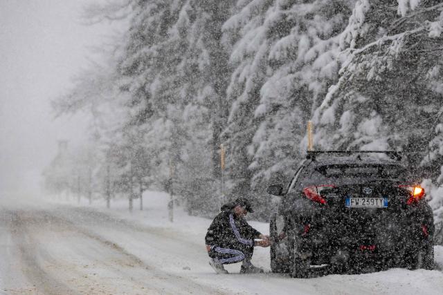 A motorist fits snowchains on his vehicle at a mountain pass road near Toblach running between the Olympic venues in Cortina and Antholz, northern Italy prior to the Milano Cortina 2026 Olympic Games, on January 25, 2026. (Photo by Odd ANDERSEN / AFP)