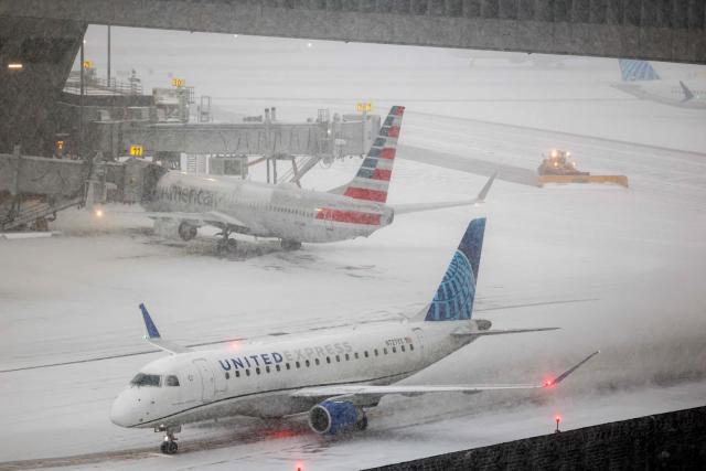 A snow removal machine is seen working while an Embraer 175 of United airlines taxies to take off on the tarmac of LaGuardia airport in New York on January 25, 2026. A massive winter storm on January 24, 2026 dumped snow and freezing rain on New Mexico and Texas as it swept across the United States towards the northeast, threatening tens of millions of Americans with blackouts, transportation chaos and bone-chilling cold. Shoppers stripped supermarket shelves as the National Weather Service (NWS) forecast huge snowfall in some areas and possibly "catastrophic" ice accumulations. (Photo by CHARLY TRIBALLEAU / AFP)