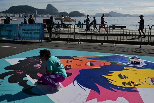 An artist paints a large canvas banner depicting one of the host cities of the Women’s World Cup at Avenida Atlantica on the seaside promenade of the iconic Copacabana beach, during the Street Art Festival within the launch of the 2027 FIFA Women's World Cup in Rio de Janeiro, Brazil on January 25, 2026. (Photo by Pablo PORCIUNCULA / AFP)