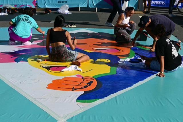 Artists paint a large canvas banner depicting one of the host cities of the Women’s World Cup at Avenida Atlantica on the seaside promenade of the iconic Copacabana beach, during the Street Art Festival within the launch of the 2027 FIFA Women's World Cup in Rio de Janeiro, Brazil on January 25, 2026. (Photo by Pablo PORCIUNCULA / AFP)