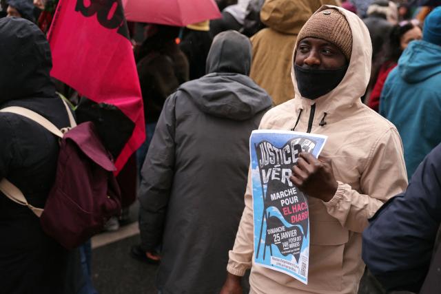 A participant holds a flyer for the march in tribute to 35-year-old El Hacen Diarra, who died in police custody at the police station of Paris's 20th arrondissement, in Paris on January 25, 2026. (Photo by Thomas SAMSON / AFP)