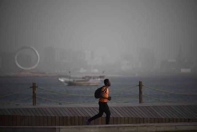 A man runs at the beach during a dust storm in Qatar's capital Doha, on January 25, 2026. (Photo by Mahmud HAMS / AFP)