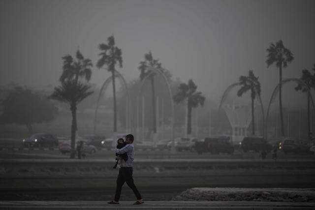A man walks holding a child during a dust storm in Qatar's capital Doha, on January 25, 2026. (Photo by Mahmud HAMS / AFP)