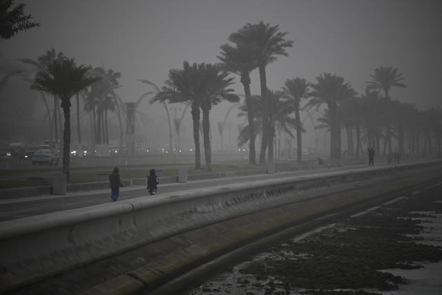 People walk during a dust storm in Qatar's capital Doha, on January 25, 2026. (Photo by Mahmud HAMS / AFP)