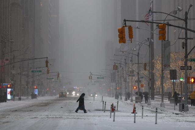 A person walks across Sixth Avenue as snow falls in the Manhattan borough of New York City on January 25, 2026. A massive winter storm on January 24 dumped snow and freezing rain from New Mexico to North Carolina as it swept across the United States towards the northeast, threatening tens of millions of Americans with blackouts, transportation chaos and bone-chilling cold. After battering the country's southwest and central areas, the storm system began to hit the heavily populated mid-Atlantic and northeastern states as a frigid air mass settled in across the nation. (Photo by CHARLY TRIBALLEAU / AFP)