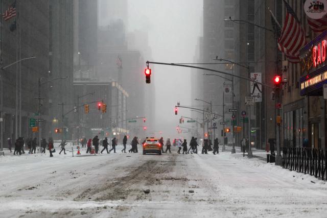 People walk across Sixth Avenue as snow falls in the Manhattan borough of New York City on January 25, 2026. A massive winter storm on January 24 dumped snow and freezing rain from New Mexico to North Carolina as it swept across the United States towards the northeast, threatening tens of millions of Americans with blackouts, transportation chaos and bone-chilling cold. After battering the country's southwest and central areas, the storm system began to hit the heavily populated mid-Atlantic and northeastern states as a frigid air mass settled in across the nation. (Photo by CHARLY TRIBALLEAU / AFP)