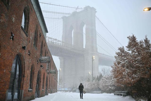 A person walks in the snow near the Brooklyn Bridge in New York City on January 25, 2026. A massive winter storm on January 24 dumped snow and freezing rain from New Mexico to North Carolina as it swept across the United States towards the northeast, threatening tens of millions of Americans with blackouts, transportation chaos and bone-chilling cold. After battering the country's southwest and central areas, the storm system began to hit the heavily populated mid-Atlantic and northeastern states as a frigid air mass settled in across the nation. (Photo by ANGELA WEISS / AFP)