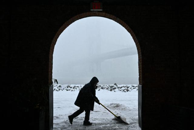 A person clears snow from a walkway near Brooklyn Bridge Park in New York City on January 25, 2026. A massive winter storm on January 24 dumped snow and freezing rain from New Mexico to North Carolina as it swept across the United States towards the northeast, threatening tens of millions of Americans with blackouts, transportation chaos and bone-chilling cold. After battering the country's southwest and central areas, the storm system began to hit the heavily populated mid-Atlantic and northeastern states as a frigid air mass settled in across the nation. (Photo by ANGELA WEISS / AFP)