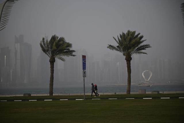 People walk along the beach during a dust storm in Qatar's capital Doha, on January 25, 2026. (Photo by Mahmud HAMS / AFP)