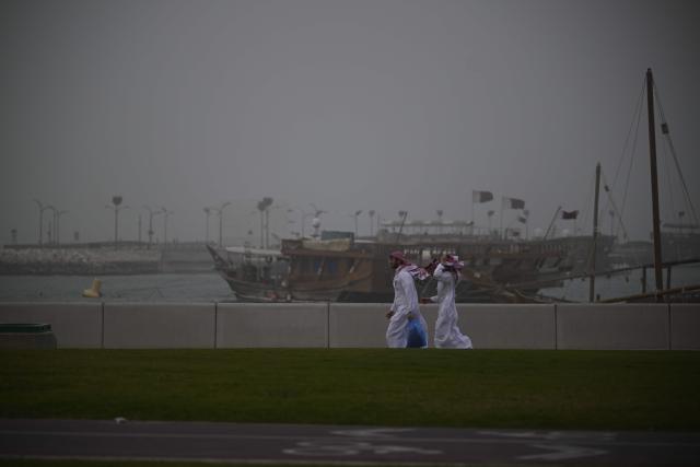 People walk during a dust storm in Qatar's capital Doha, on January 25, 2026. (Photo by Mahmud HAMS / AFP)