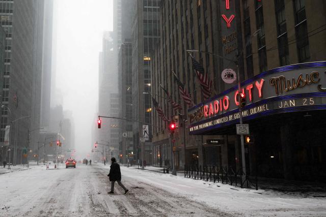 A person walks across Sixth Avenue as snow falls in the Manhattan borough of New York City on January 25, 2026. A massive winter storm on January 24 dumped snow and freezing rain from New Mexico to North Carolina as it swept across the United States towards the northeast, threatening tens of millions of Americans with blackouts, transportation chaos and bone-chilling cold. After battering the country's southwest and central areas, the storm system began to hit the heavily populated mid-Atlantic and northeastern states as a frigid air mass settled in across the nation. (Photo by CHARLY TRIBALLEAU / AFP)