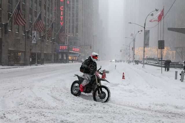 A person rides a motor bike in the snow on Sixth Avenue in New York City on January 25, 2026. A massive winter storm on January 24 dumped snow and freezing rain from New Mexico to North Carolina as it swept across the United States towards the northeast, threatening tens of millions of Americans with blackouts, transportation chaos and bone-chilling cold. After battering the country's southwest and central areas, the storm system began to hit the heavily populated mid-Atlantic and northeastern states as a frigid air mass settled in across the nation. (Photo by CHARLY TRIBALLEAU / AFP)