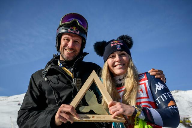 (FILES) First-placed US Lindsey Vonn (R) holds her trophy as she poses with her coach and former Norway's skier Aksel Lund Svindal (L) following the podium ceremony for the women's downhill race during the FIS Alpine Ski World Cup 2025-2026, in St Moritz, south-eastern Switzerland on December 12, 2025. US ski star Lindsey Vonn has defied age and injury to make one of the most remarkable comebacks in Olympic history, the latest chapter in a storied career of memorable highs and crushing setbacks. Vonn will be 41 when she takes to the slope of Cortina d'Ampezzo next month for her fifth Olympics. She retired after the 2019 world championships in Are but made what she dubbed a "crazy" comeback last winter. (Photo by Fabrice COFFRINI / AFP)