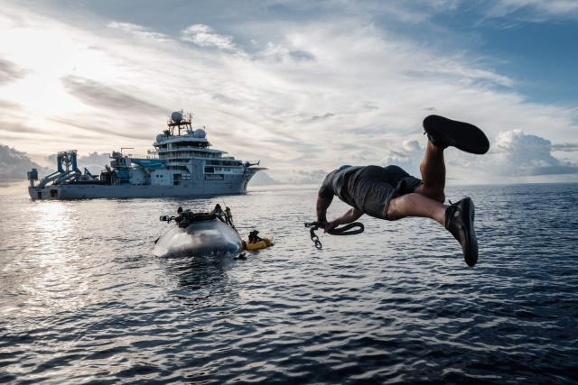 TOPSHOT - This photo taken on January 9, 2026 shows the crew of the OceanXplorer, a research vessel operated by the marine non-profit OceanX, jumping into the sea from a boat to swim toward a surfaced submersible and attach a recovery line in the waters off Sulawesi island. A dome-fronted submersible sinks beneath the waves off Indonesia, heading nearly 1,000 metres down to the realm of purple-frilled corals and bioluminescent shrimp. This month, AFP boarded one of two submersibles belonging to OceanX, a non-profit founded by billionaire Ray Dalio and his son that works with scientists on its OceanXplorer ship to study the marine world. (Photo by YASUYOSHI CHIBA / AFP) / To go with 'INDONESIA-OCEANX-OCEANS-ENVIRONMENT-RESEARCH-SCIENCE' by Sara HUSSEIN