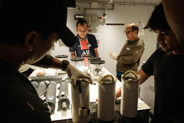 This photo taken on January 9, 2026 shows Indonesian marine scientists discussing deep-sea specimens collected by a submersible on the OceanXplorer, a research vessel operated by the marine non-profit OceanX, in the waters off Sulawesi island. A dome-fronted submersible sinks beneath the waves off Indonesia, heading nearly 1,000 metres down to the realm of purple-frilled corals and bioluminescent shrimp. This month, AFP boarded one of two submersibles belonging to OceanX, a non-profit founded by billionaire Ray Dalio and his son that works with scientists on its OceanXplorer ship to study the marine world. (Photo by YASUYOSHI CHIBA / AFP) / To go with 'INDONESIA-OCEANX-OCEANS-ENVIRONMENT-RESEARCH-SCIENCE' by Sara HUSSEIN