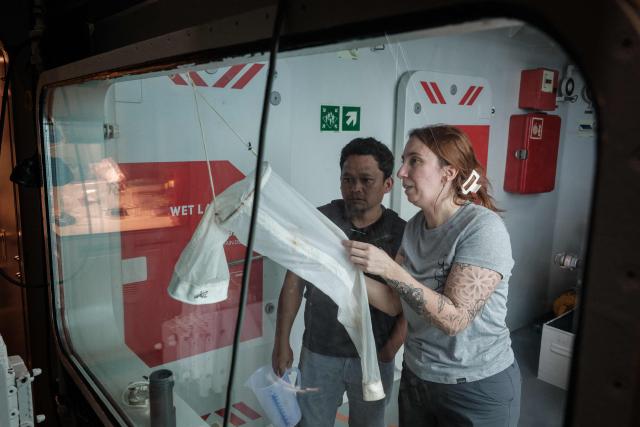 This photo taken on January 9, 2026, shows Larissa Fruehe (R), a German environmental DNA (eDNA) scientist, discussing methods for filtering plankton from seawater samples with an Indonesian marine scientist on the OceanXplorer, a research vessel operated by the marine non-profit OceanX, in waters off Sulawesi island. A dome-fronted submersible sinks beneath the waves off Indonesia, heading nearly 1,000 metres down to the realm of purple-frilled corals and bioluminescent shrimp. This month, AFP boarded one of two submersibles belonging to OceanX, a non-profit founded by billionaire Ray Dalio and his son that works with scientists on its OceanXplorer ship to study the marine world. (Photo by YASUYOSHI CHIBA / AFP) / To go with: INDONESIA-OCEANX-OCEANS-ENVIRONMENT-RESEARCH-SCIENCE, by Sara HUSSEIN