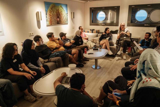 This photo taken on January 11, 2026, shows Larissa Fruehe (2nd R), a German environmental DNA (eDNA) scientist, discussing plans for the following day with Indonesian scientists and crew members on the OceanXplorer, a research vessel operated by the marine non-profit OceanX, in waters off Sulawesi island. A dome-fronted submersible sinks beneath the waves off Indonesia, heading nearly 1,000 metres down to the realm of purple-frilled corals and bioluminescent shrimp. This month, AFP boarded one of two submersibles belonging to OceanX, a non-profit founded by billionaire Ray Dalio and his son that works with scientists on its OceanXplorer ship to study the marine world. (Photo by YASUYOSHI CHIBA / AFP) / To go with: INDONESIA-OCEANX-OCEANS-ENVIRONMENT-RESEARCH-SCIENCE, by Sara HUSSEIN