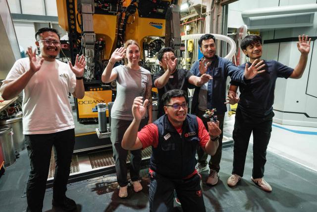 This photo taken on January 9, 2026, shows Larissa Fruehe (2L), a German environmental DNA (eDNA) scientist, recording a commemorative video with Indonesian marine scientists in front of a remotely operated vehicle (ROV) on the OceanXplorer, a research vessel operated by the marine non-profit OceanX, in waters off Sulawesi island. A dome-fronted submersible sinks beneath the waves off Indonesia, heading nearly 1,000 metres down to the realm of purple-frilled corals and bioluminescent shrimp. This month, AFP boarded one of two submersibles belonging to OceanX, a non-profit founded by billionaire Ray Dalio and his son that works with scientists on its OceanXplorer ship to study the marine world. (Photo by YASUYOSHI CHIBA / AFP) / To go with: INDONESIA-OCEANX-OCEANS-ENVIRONMENT-RESEARCH-SCIENCE, by Sara HUSSEIN