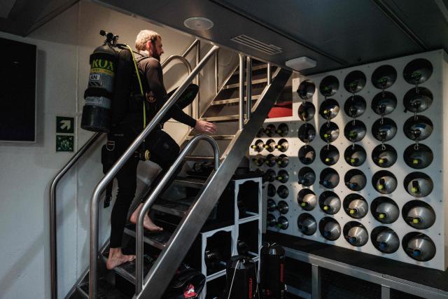 This photo taken on January 12, 2026, shows a dive crew carrying diving gear on the OceanXplorer, a research vessel operated by the marine non-profit OceanX, for a deep-sea mission in the waters off Sulawesi island. A dome-fronted submersible sinks beneath the waves off Indonesia, heading nearly 1,000 metres down to the realm of purple-frilled corals and bioluminescent shrimp. This month, AFP boarded one of two submersibles belonging to OceanX, a non-profit founded by billionaire Ray Dalio and his son that works with scientists on its OceanXplorer ship to study the marine world. (Photo by YASUYOSHI CHIBA / AFP) / To go with: INDONESIA-OCEANX-OCEANS-ENVIRONMENT-RESEARCH-SCIENCE, by Sara HUSSEIN