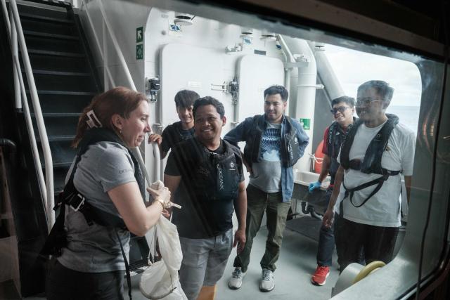 This photo taken on January 9, 2026, shows Larissa Fruehe (L), a German environmental DNA (eDNA) scientist, discussing methods for filtering plankton from seawater samples with Indonesian marine scientists on the OceanXplorer, a research vessel operated by the marine non-profit OceanX, in waters off Sulawesi island. A dome-fronted submersible sinks beneath the waves off Indonesia, heading nearly 1,000 metres down to the realm of purple-frilled corals and bioluminescent shrimp. This month, AFP boarded one of two submersibles belonging to OceanX, a non-profit founded by billionaire Ray Dalio and his son that works with scientists on its OceanXplorer ship to study the marine world. (Photo by YASUYOSHI CHIBA / AFP) / To go with: INDONESIA-OCEANX-OCEANS-ENVIRONMENT-RESEARCH-SCIENCE, by Sara HUSSEIN