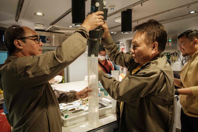 This photo taken on January 10, 2026, shows Alex Masengi (C), a coelacanth researcher from Sam Ratulangi University, transferring seawater samples collected from the deep sea into separate containers while preparing to search for coelacanth DNA on rthe OceanXplorer, a research vessel operated by the marine non-profit OceanX, in the waters off Sulawesi island. A dome-fronted submersible sinks beneath the waves off Indonesia, heading nearly 1,000 metres down to the realm of purple-frilled corals and bioluminescent shrimp. This month, AFP boarded one of two submersibles belonging to OceanX, a non-profit founded by billionaire Ray Dalio and his son that works with scientists on its OceanXplorer ship to study the marine world. (Photo by YASUYOSHI CHIBA / AFP) / To go with: INDONESIA-OCEANX-OCEANS-ENVIRONMENT-RESEARCH-SCIENCE, by Sara HUSSEIN