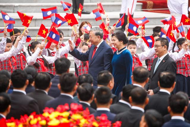 Vietnam's Communist Party General Secretary To Lam (C) and his wife Ngo Phuong Ly (C-R) wave to children ahead of a welcoming ceremony at the presidential palace in Hanoi on January 26, 2026. (Photo by LUONG THAI LINH / POOL / AFP)
