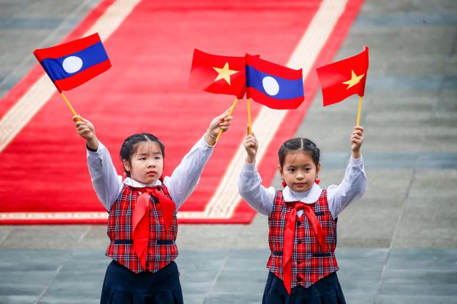 Children wave flags of Vietnam and Laos ahead a welcoming ceremony at the presidential palace in Hanoi on January 26, 2026. (Photo by LUONG THAI LINH / POOL / AFP)