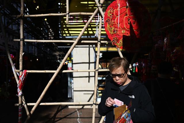 A man handles currency after a purchase while walking past bamboo scaffolding in the Sham Shui Po district of Hong Kong on January 26, 2026. (Photo by Peter PARKS / AFP)