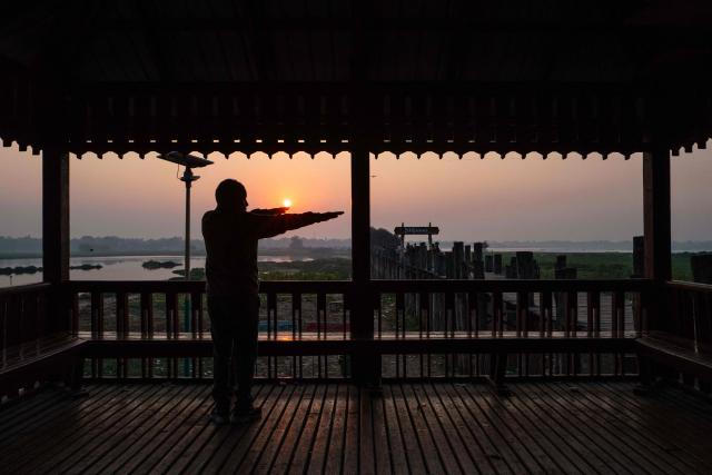 TOPSHOT - A man stretches at a lookout point next to the U Bein bridge, which spans the Taungthaman Lake, as the sun rises in Mandalay on January 26, 2026. (Photo by ANTHONY WALLACE / AFP)