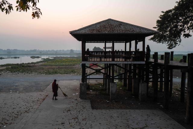 A monk sweeps leaves next to the U Bein bridge in Mandalay on January 26, 2026. (Photo by ANTHONY WALLACE / AFP)