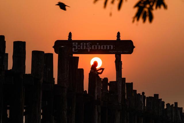 TOPSHOT - A man is silhouetted by the rising sun as he takes a photo on the U Bein bridge in Mandalay on January 26, 2026. (Photo by ANTHONY WALLACE / AFP)