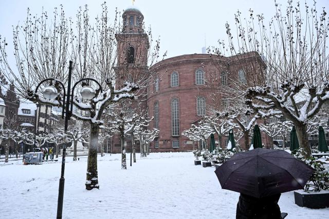A woman under her unmbrella walks on the snow-covered square in front of St Paul's Church in Frankfurt am Main, western Germany, on January 26, 2026 as the air temperature reached 1 degrees Celsius above zero. (Photo by Kirill KUDRYAVTSEV / AFP)