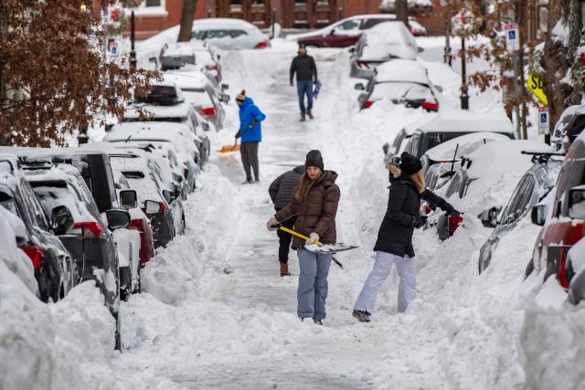 People shovel snow along a residential street in the Charlestown neighborhood in Boston, Massachusetts on January 26, 2026. A monster storm barreling across the United States had killed at least 11 people on Monday, prompting warnings to stay off the roads, mass flight cancelations and power outages after a weekend of misery. The storm dumped snow, sleet and freezing rain across swathes of the country from Texas to New England, with temperatures set to fall dangerously low this week. (Photo by Joseph Prezioso / AFP)