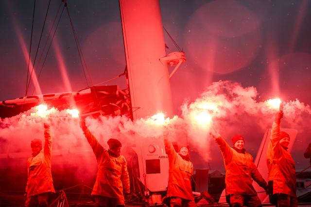 French skipper Alexia Barrier and crew members celebrate holding lit flares upon their arrival at Brest harbour on the Ultim multihull Idec Sport after crossing the finish line of the Jules Verne Trophy, off the coast of Brest, Brittany, on January 26, 2026. French skipper Alexia Barrier (The Famous Project) and her six crew members completed on January 26, 2026, off the coast of Brest, the first non-stop round-the-world voyage in a maxi-trimaran with an all-female crew, her team announced. (Photo by Loic VENANCE / AFP)