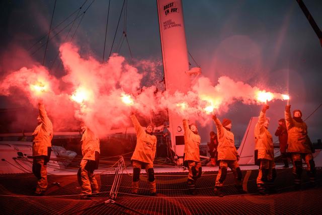 French skipper Alexia Barrier and crew members celebrate holding lit flares upon their arrival at Brest harbour on the Ultim multihull Idec Sport after crossing the finish line of the Jules Verne Trophy, off the coast of Brest, Brittany, on January 26, 2026. French skipper Alexia Barrier (The Famous Project) and her six crew members completed on January 26, 2026, off the coast of Brest, the first non-stop round-the-world voyage in a maxi-trimaran with an all-female crew, her team announced. (Photo by Loic VENANCE / AFP)