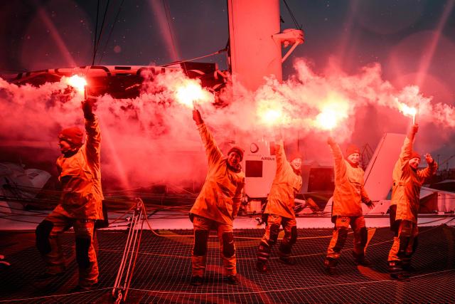 French skipper Alexia Barrier and crew members celebrate holding lit flares upon their arrival at Brest harbour on the Ultim multihull Idec Sport after crossing the finish line of the Jules Verne Trophy, off the coast of Brest, Brittany, on January 26, 2026. French skipper Alexia Barrier (The Famous Project) and her six crew members completed on January 26, 2026, off the coast of Brest, the first non-stop round-the-world voyage in a maxi-trimaran with an all-female crew, her team announced. (Photo by Loic VENANCE / AFP)