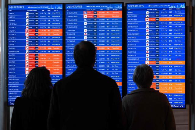 Travelers look at a flight status board as flights are delayed and cancelled following a significant winter storm at Ronald Reagan Washington National Airport in Arlington, Virginia, January 26, 2026. Millions of Americans were facing dangerously cold temperatures in the wake of a massive winter storm that whipped snow and ice across the country, knocking out power and paralyzing transportation. A frigid, potentially life-threatening Arctic air mass threatened to delay clean-up as municipalities from New Mexico to Maine tried to dig out following the storm, which dropped a vicious cocktail of heavy snow and wind along with freezing rain and sleet. (Photo by SAUL LOEB / AFP)